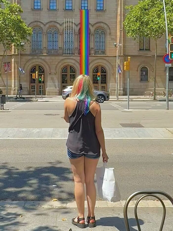 Photographer captures perfectly timed coincidence in Barcelona, aligning a woman's rainbow hair with a colorful pole.