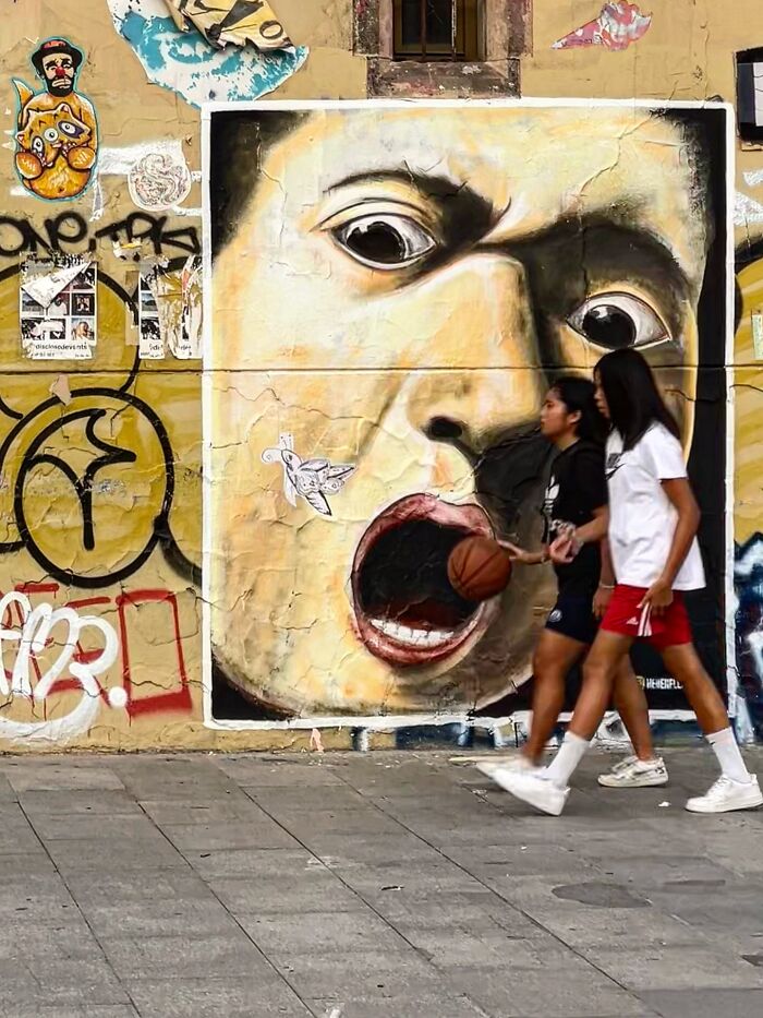 Perfectly timed coincidences in Barcelona: two girls playing basketball appear to feed a mural's open mouth.