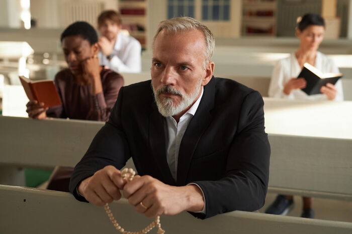 Man in a suit holding rosary beads in a church; examples of dumb reasons people got fired.
