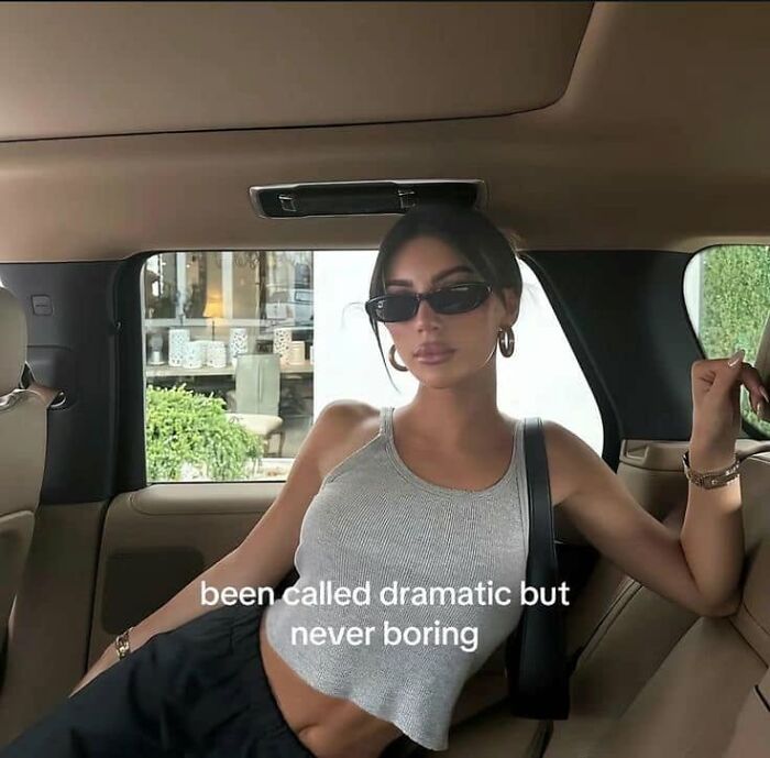 A woman in a car with the text been called dramatic but never boring, a funny post about being a woman.