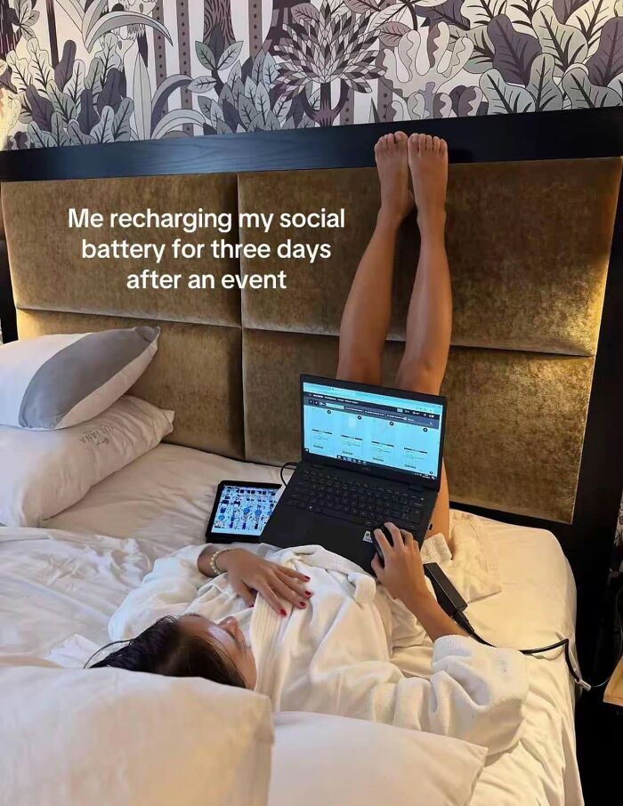 A woman in a robe with legs up, on a laptop in bed, captioned recharging social battery after an event, a funny post about being a woman.