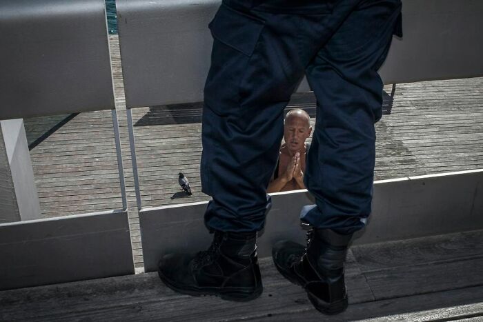 Man in military uniform standing over a man praying, a serendipitous moment captured in everyday life by a street photographer.