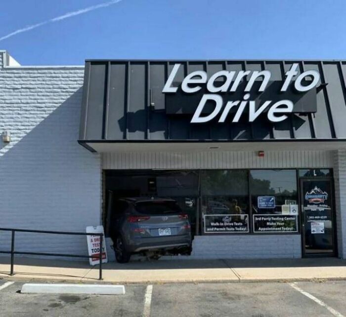 A car crashed into a 'Learn to Drive' building, exemplifying the cultural decline into idiocy.
