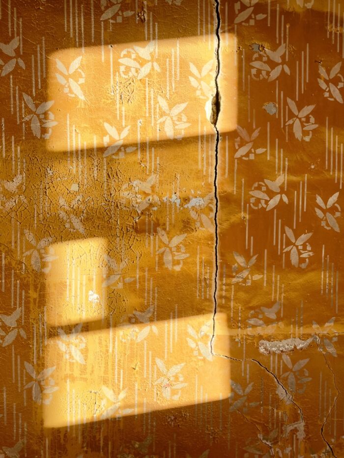 Sunlight creates rectangular shadows on a cracked, patterned yellow wall, an extraordinary winning iPhone photo.