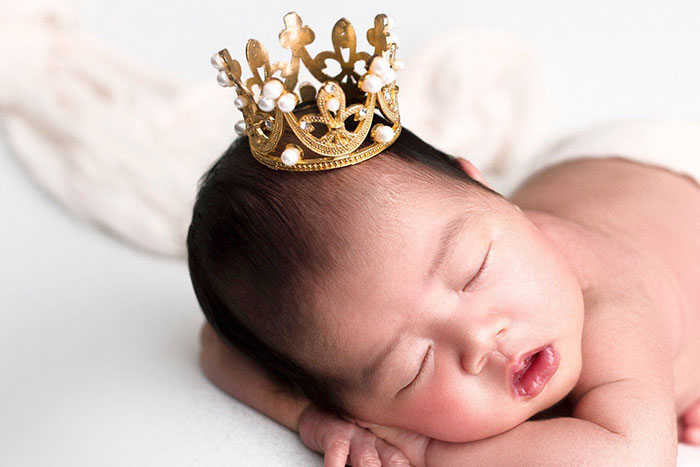 A sleeping baby wearing a small golden crown, symbolizing the innocence before knowing about unfortunate names.