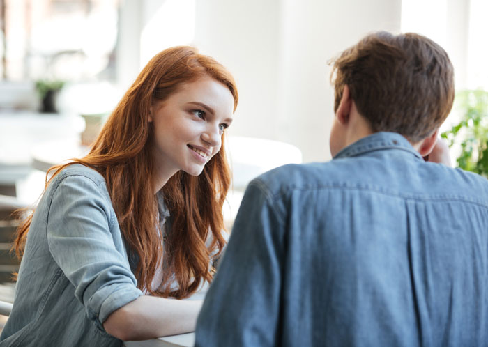 A woman with red hair looking at a man, sharing a moment that could lead to clever comebacks.