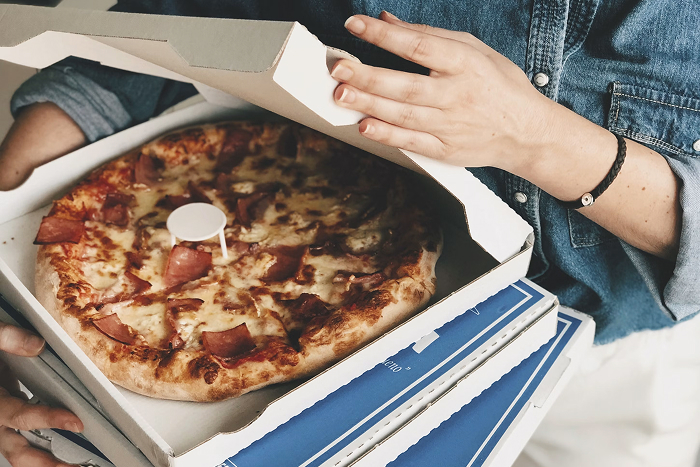 Hands opening a pizza box with a hot pizza inside, a common scenario for infuriating mansplaining.