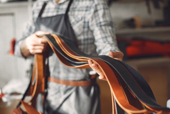 A craftsman holding various leather straps, showcasing surprisingly affordable custom leather goods.