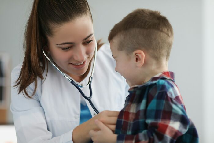 A female doctor examining a smiling boy with a stethoscope, related to kids questions about health.