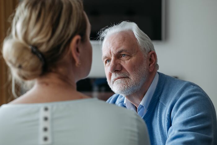 An older man with a serious expression looking at a woman, discussing their age-gap relationships.