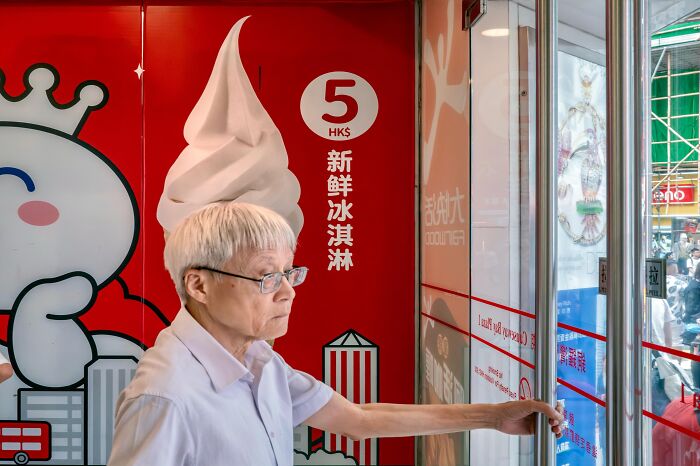 An elderly person stands in front of a giant ice cream cone graphic, creating a humorous street coincidence.