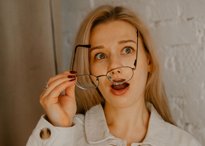 A surprised woman holding glasses, suggesting a moment where reality break.