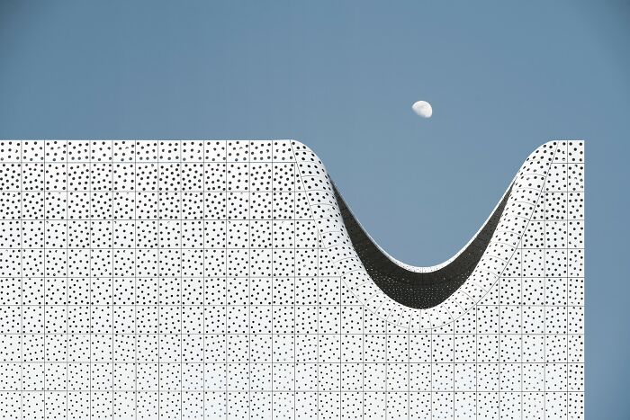 A unique architectural structure with a wavy black and white dotted pattern against a blue sky with the moon. reFocus Contest photo.