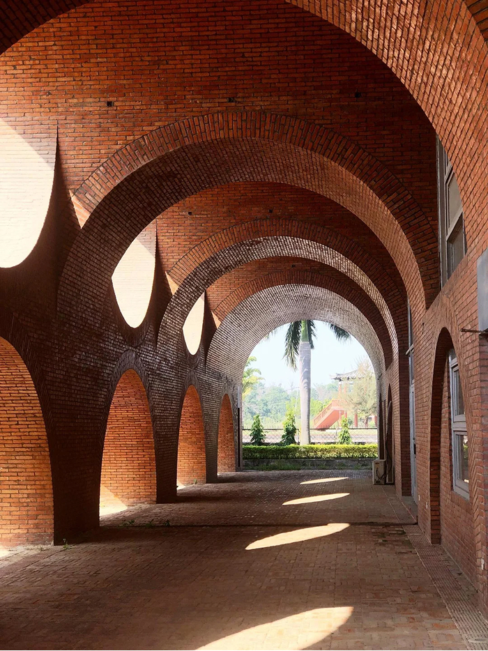 A beautiful modern architecture design with brick arches creating a long, shaded walkway leading to an outdoor area.