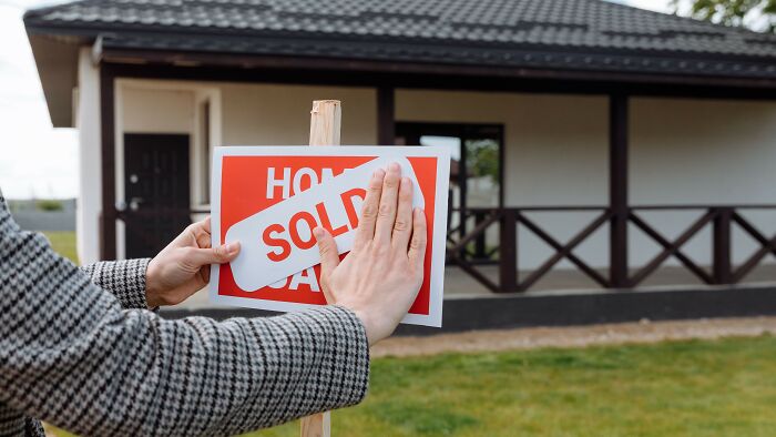 Hands putting a SOLD sign on a post in front of a house, showcasing a scenario where people might have overreacted.