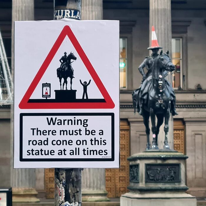 Absurd signs: A sign with a warning about a road cone on a statue.