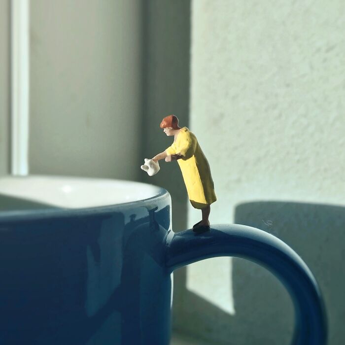 Artist Derrick Lin diorama set: A tiny figure on a blue mug, watering an invisible plant.