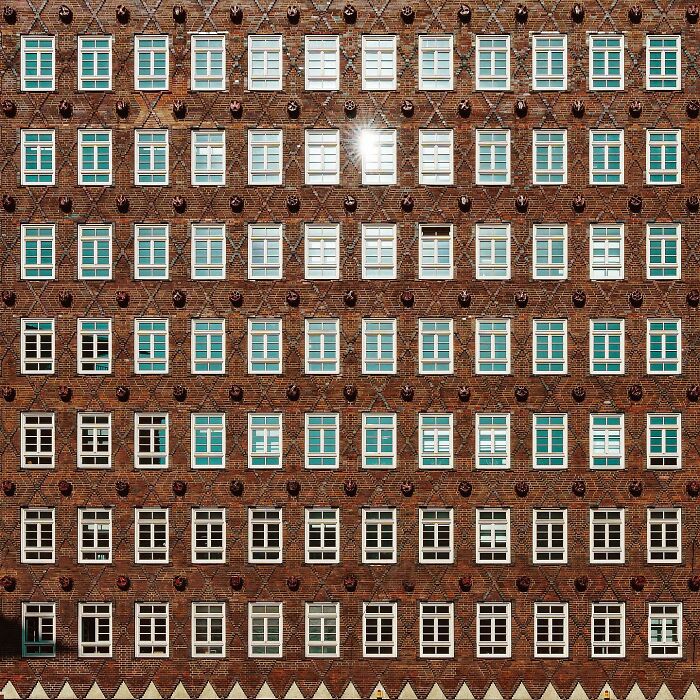 A precisely composed image of an architectural location, featuring a brick facade with a grid of windows, one reflecting sunlight.