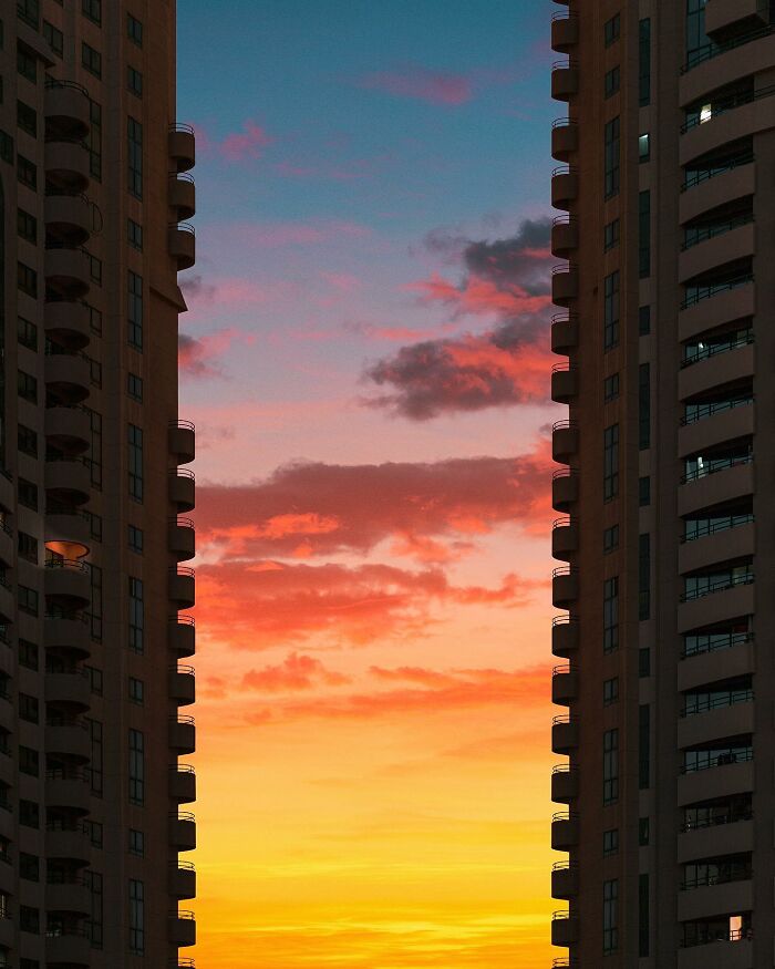 A photographer captures a perfectly composed image of two tall buildings framing a vibrant sunset with orange, pink, and blue clouds.