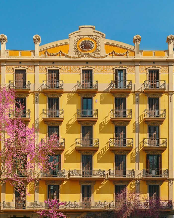 A vibrant yellow architectural location building with rows of balconies, adorned with intricate details and pink flowering trees.