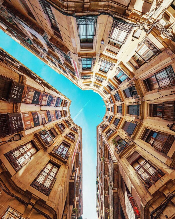 An architectural location seen from below, showcasing a narrow courtyard of buildings against a bright blue sky.