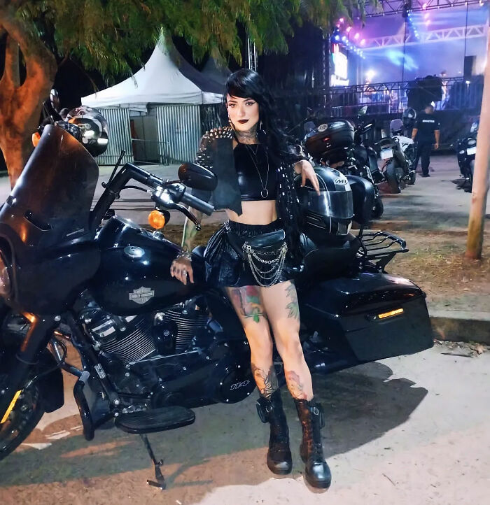 A goth influencer posing next to a motorcycle on a countryside road at night. A goth influencer posing next to a motorcycle on a countryside road at night.