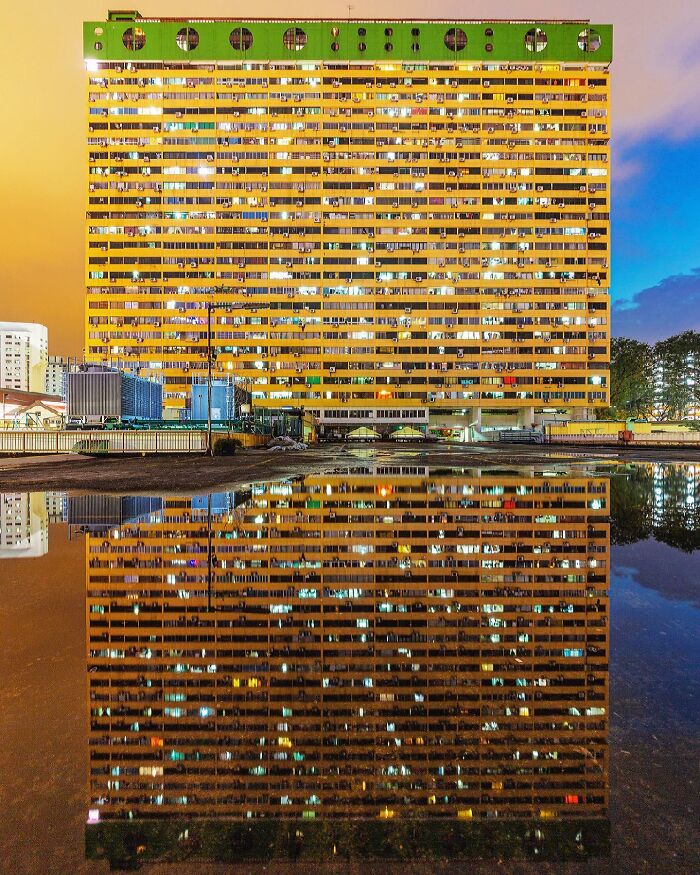 Tall, illuminated architectural building reflected in a puddle at dusk, creating a stunning symmetrical image of architectural locations.