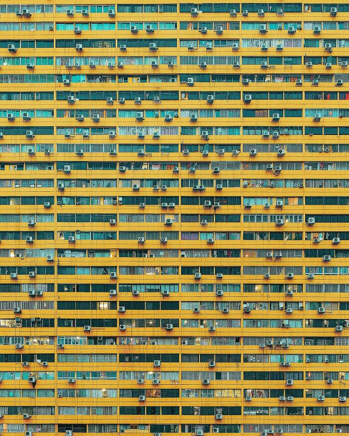 A dense pattern of windows and air conditioning units on a bright yellow building, showcasing architectural locations.