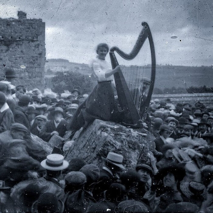 A historical photo of a woman playing a harp on a rock, surrounded by a crowd, telling incredible stories.
