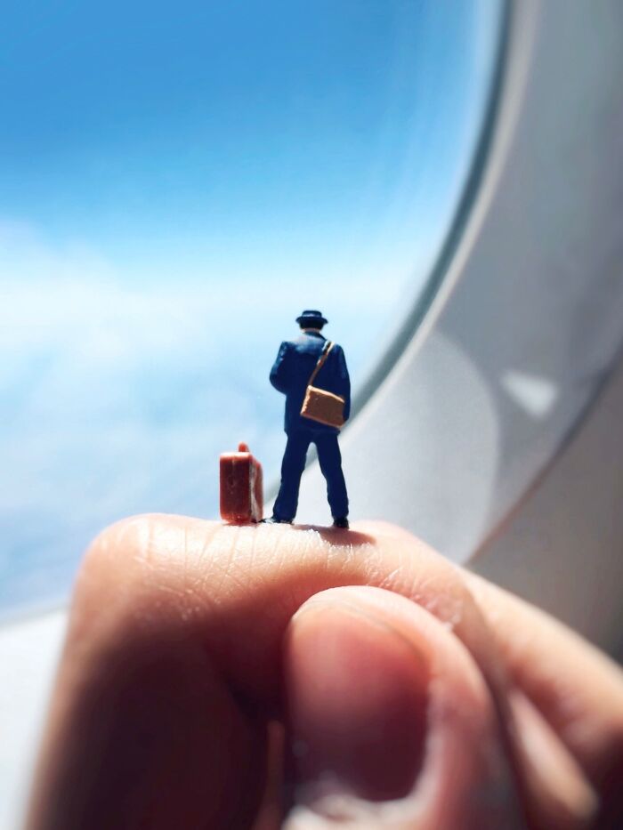Artist Derrick Lin diorama set: A miniature traveler with luggage looking out an airplane window.