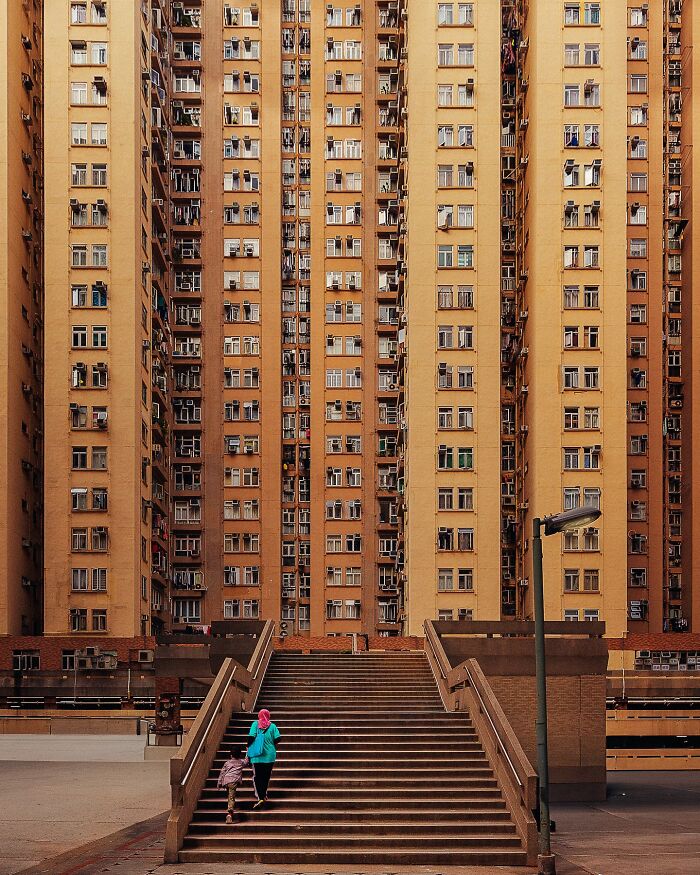 A perfectly composed image of people walking up stairs in front of a massive, symmetrical apartment building.