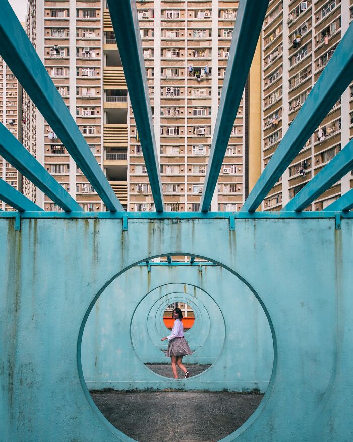 A perfectly composed image of a woman standing in a circular blue architectural tunnel, with tall buildings in the background.