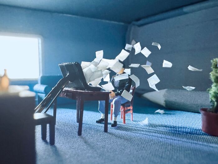 Artist Derrick Lin diorama set: A tiny person at a desk with papers flying, creating an intricate scene.
