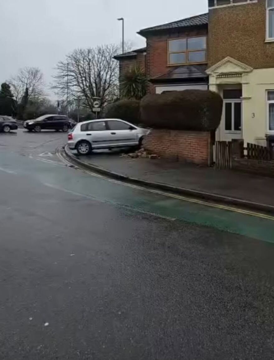 A silver hatchback crashed into a brick wall next to a house, damaging the wall and the car, a rough day behind the wheel.