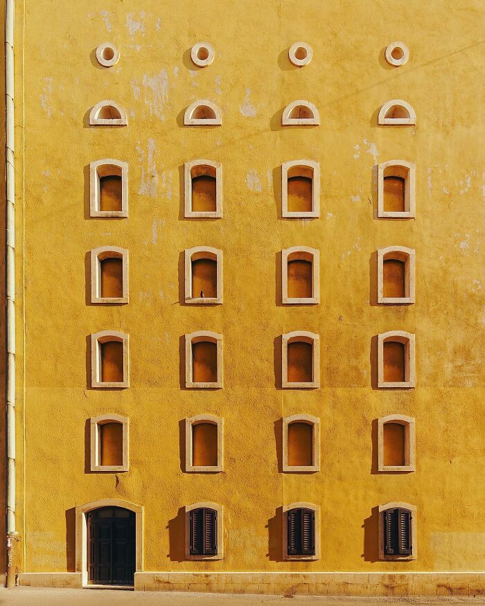 A photographer captures a perfectly composed image of a yellow architectural location with symmetrical windows and a dark door.