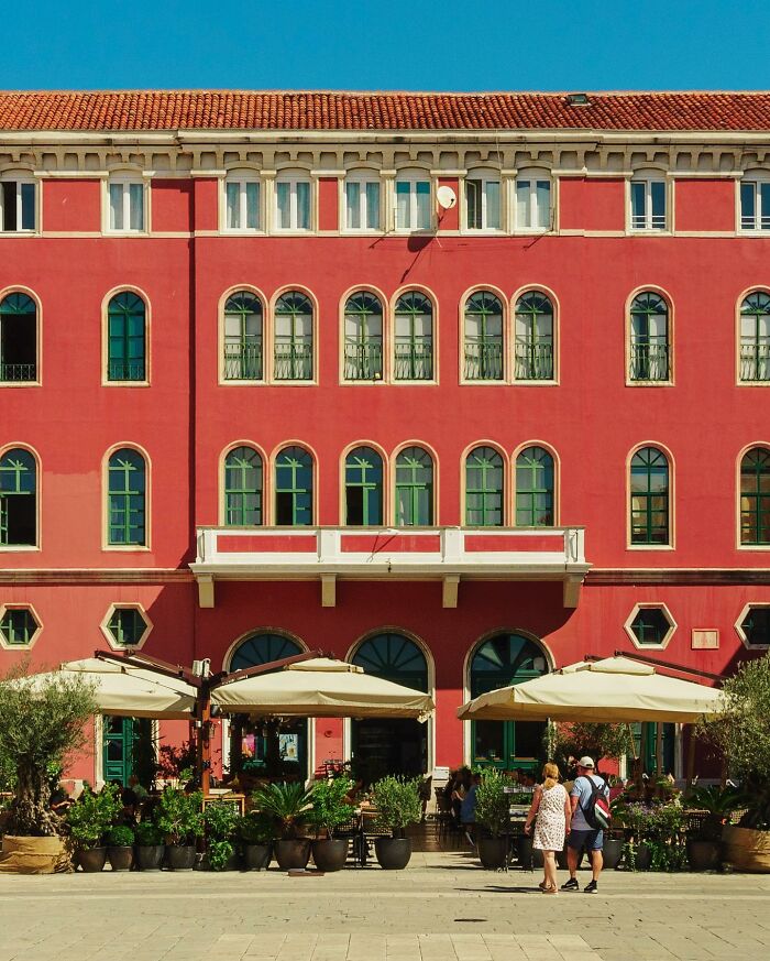 A photographer captures a perfectly composed image of a vibrant red architectural location with green windows and a cafe below.