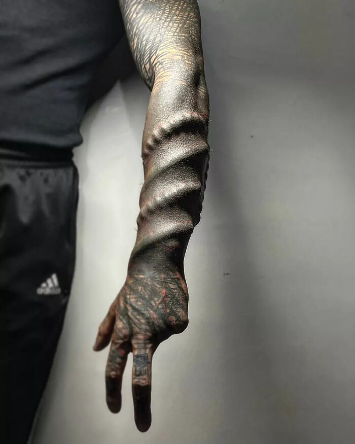 A detailed view of the Black Alien man's arm, featuring spiral textured skin and intricate tattoos. A detailed view of the Black Alien man's arm, featuring spiral textured skin and intricate tattoos.