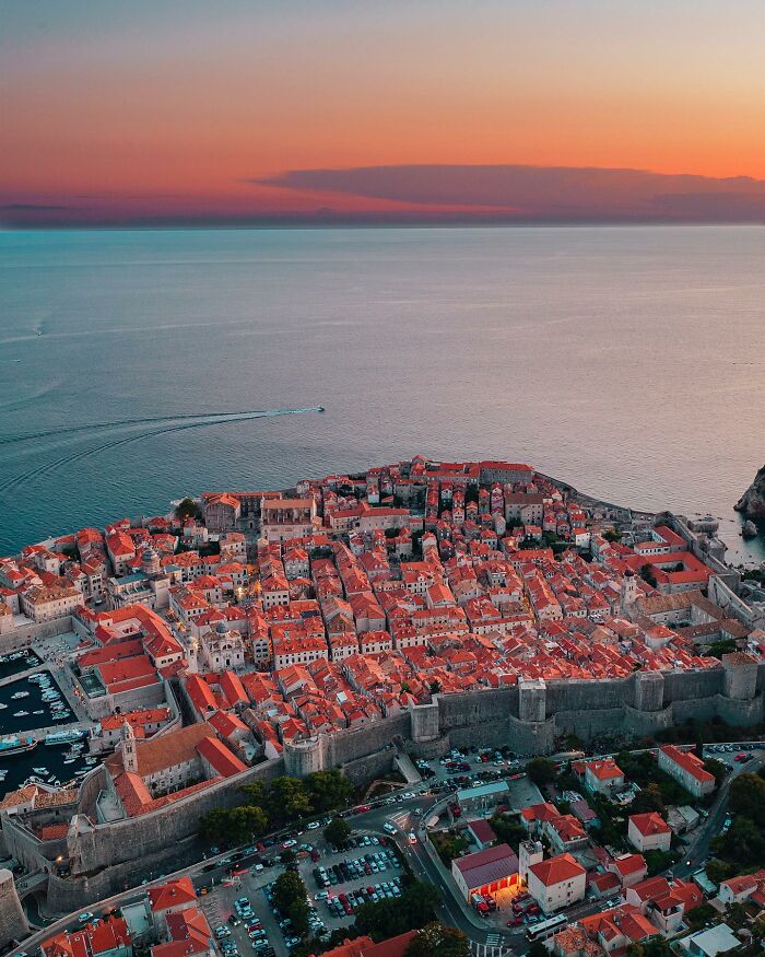 An aerial view of an ancient city with red roofs beside the ocean at sunset, a stunning architectural location.