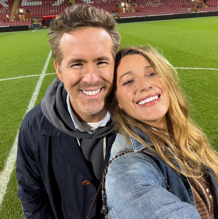 Ryan Reynolds and Blake Lively smiling at a stadium, despite Hollywood backlash rumors.