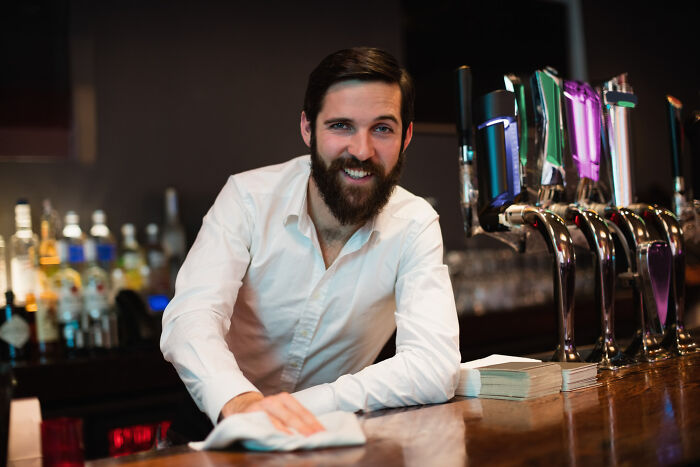A bearded bartender cleaning a bar, showing jobs guys have that make women swipe left.