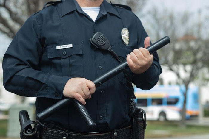 Close-up of a police officer in uniform holding a baton, relevant to MIL calling the cops to evict DIL.