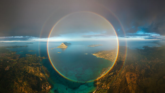 Spectacular aerial photograph showcasing a circular rainbow over a vast ocean with distant islands, awarded at the Aerial Photographer of the Year competition.