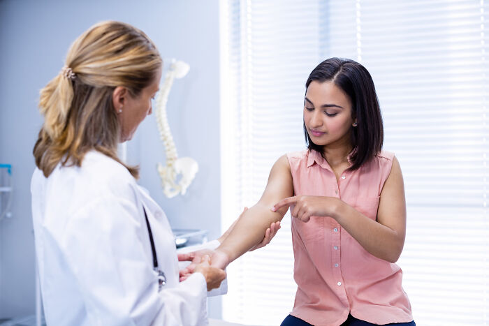A medical industry doctor examines a patient's arm, pointing at an area of concern in a bright examination room.