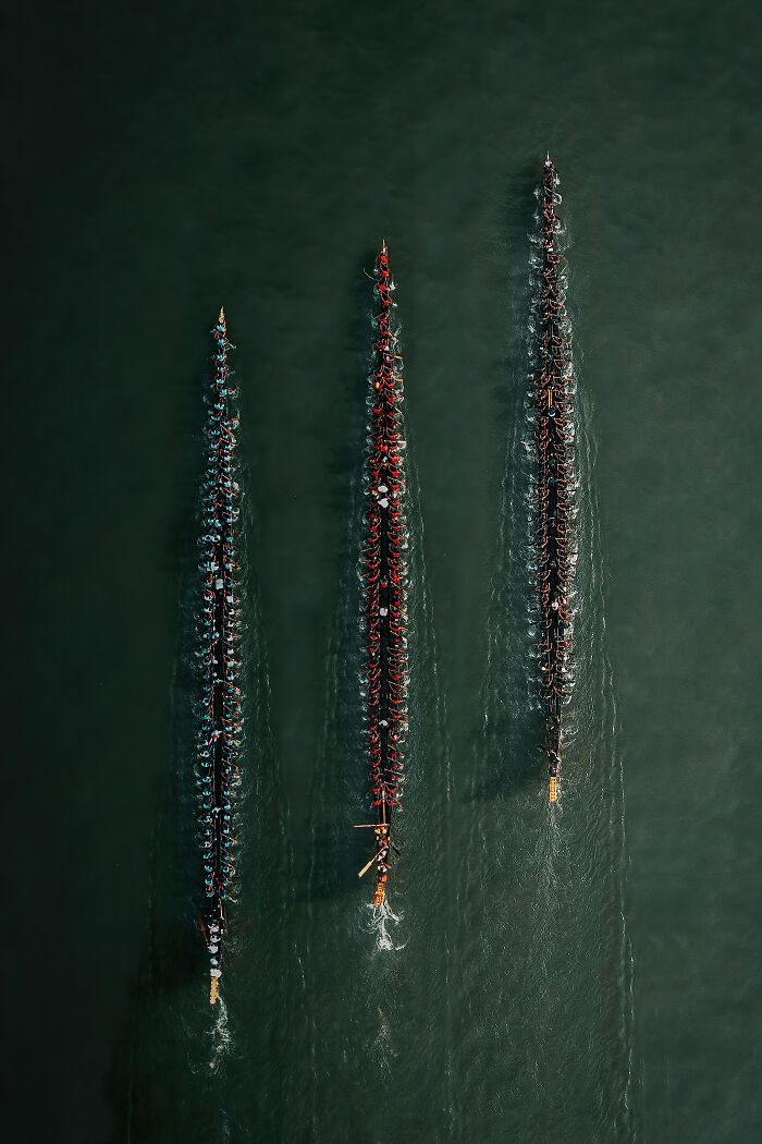 Spectacular Aerial Photographer of the Year photo showcasing three long boats with many paddlers in dark water.
