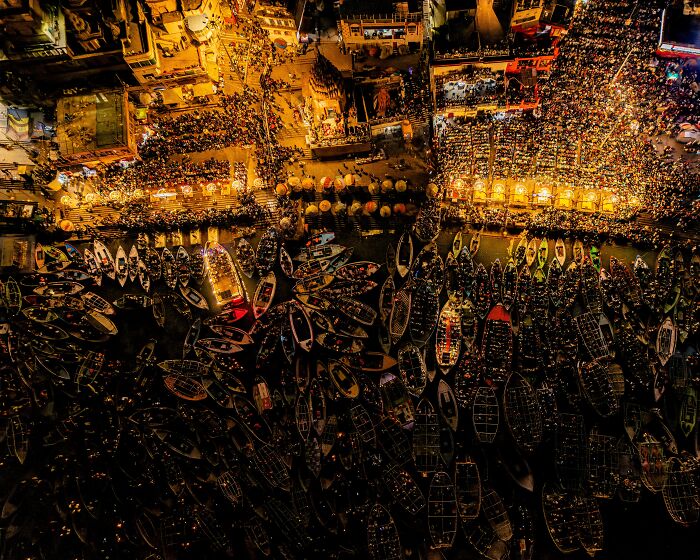 Spectacular aerial photograph of a bustling night scene with illuminated boats and crowds along a river, awarded at the Aerial Photographer of the Year competition.