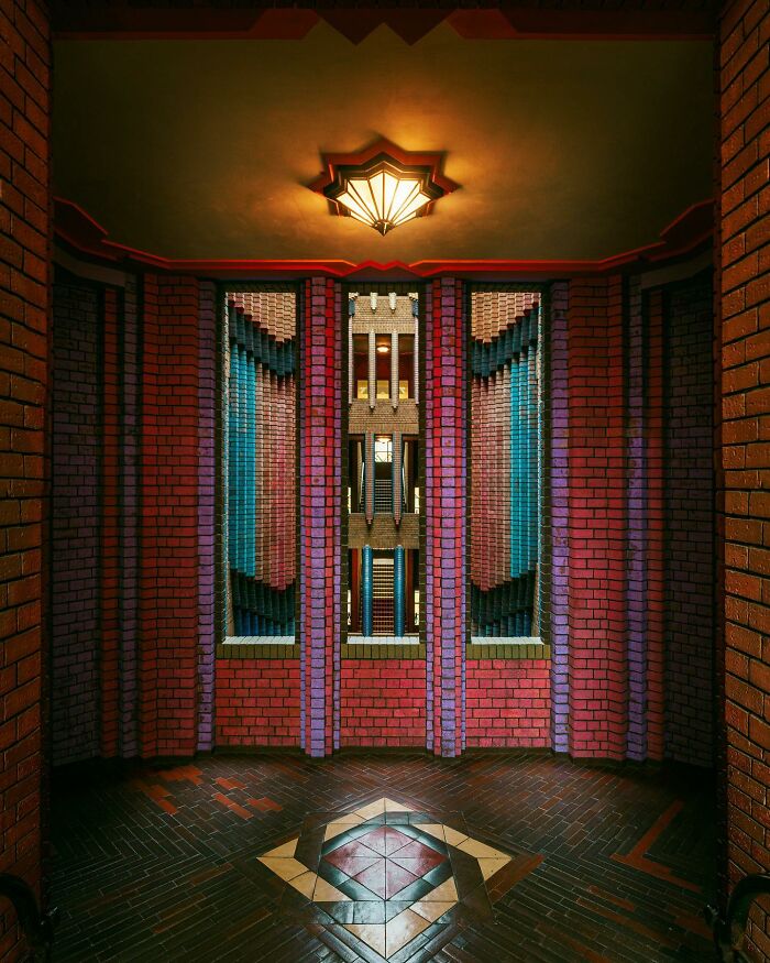 An interior view of a room with brick walls in red and purple hues, featuring a patterned floor and windows, showcasing architectural locations.