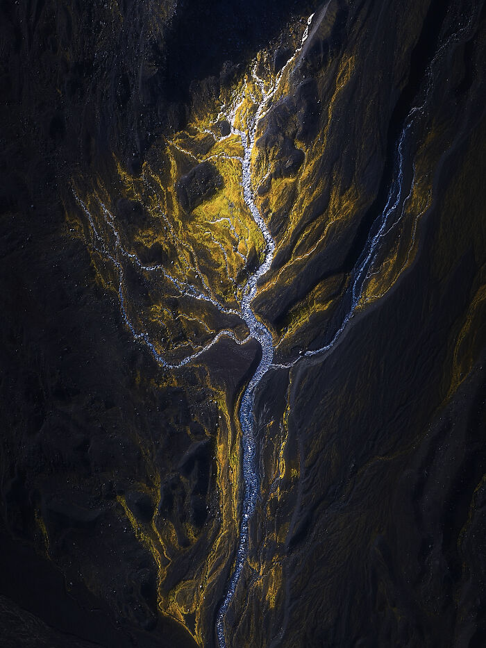 An aerial photographer captures a winding river flowing through dark terrain, illuminated by golden patches.