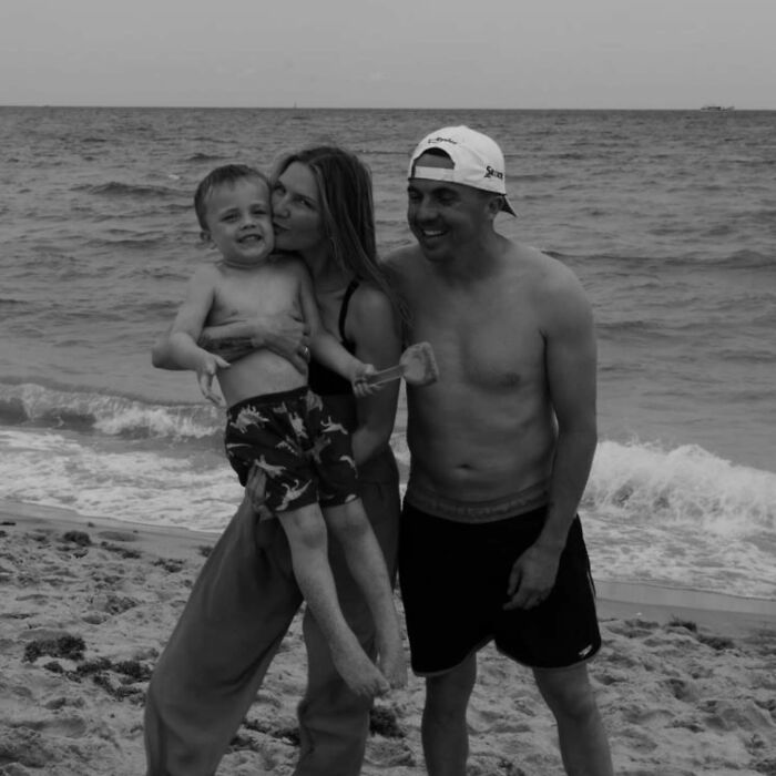 Malcolm In The Middle star, wife Paige, and their child on a beach in a black and white photo. Family by the ocean.