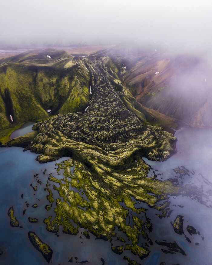 Spectacular aerial photograph of a moss-covered volcanic landscape meeting a vibrant blue lake, awarded at the Aerial Photographer of the Year competition.