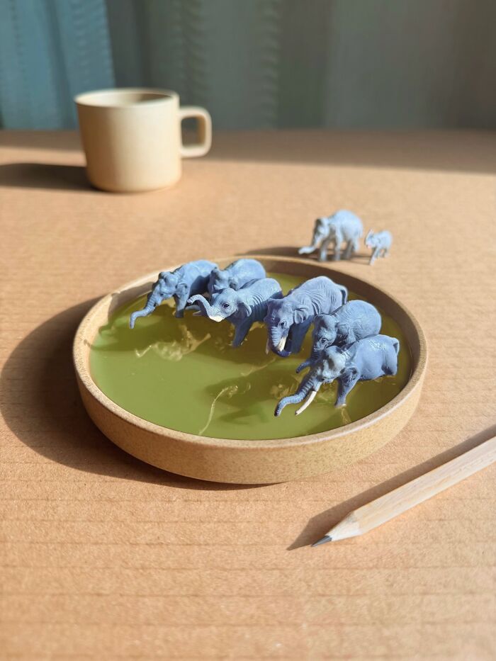 Artist Derrick Lin diorama set: Miniature elephants in a green puddle on a coaster, an intricate diorama.